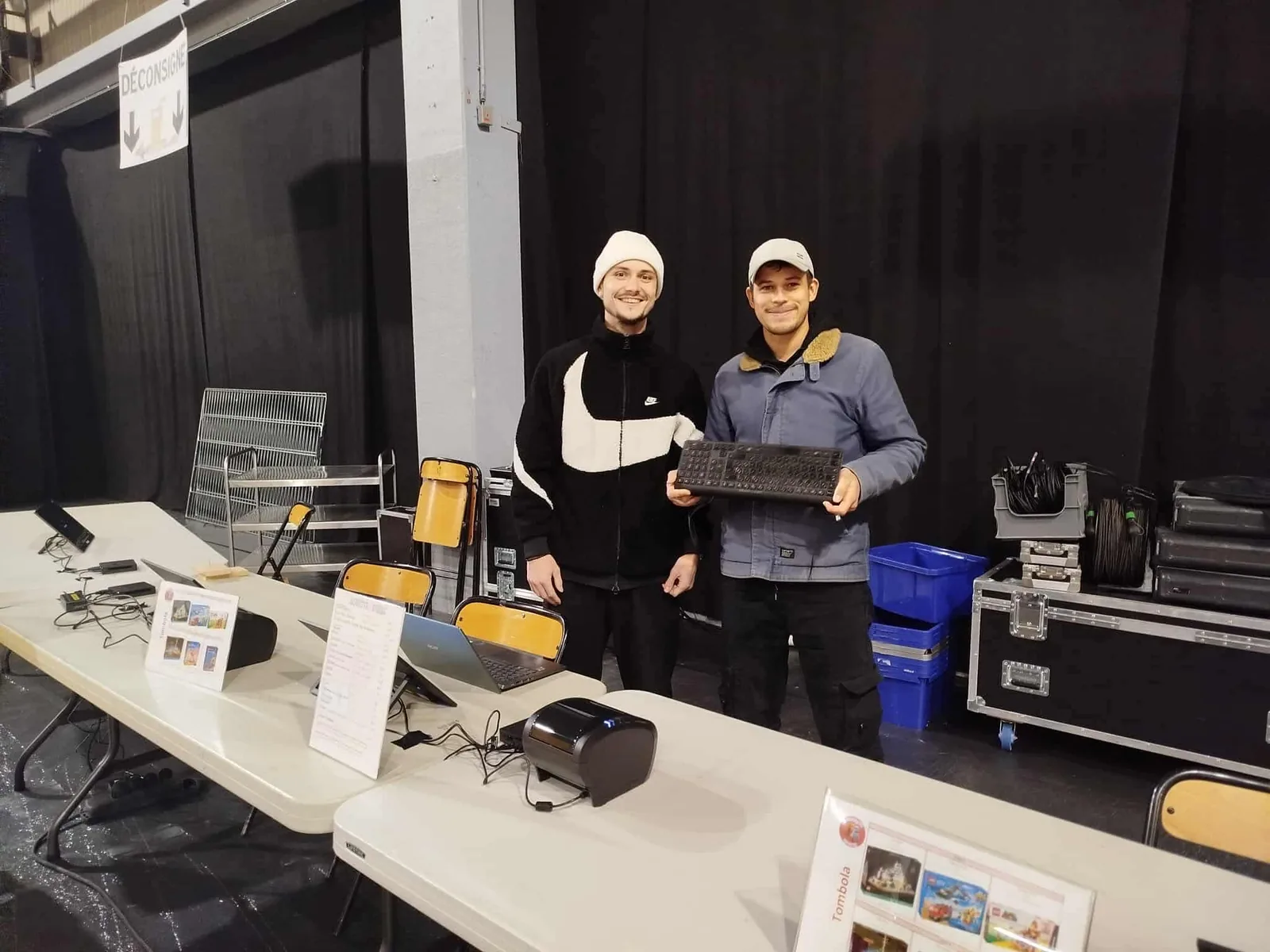 Two people standing behind folding tables with tablets, laptops and a thermal receipt printer, setting up points of sale in an event hall
